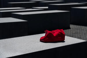 Zdjęcie w szarej tonacji. Na pierwszym planie jedyny kolorystyczny element - czerwony materiał leżący na prostokątnym, gładkim pomniku.
