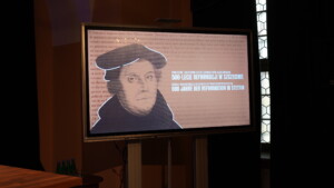 Ekran z wyświetlanym plakatem konferencji Społeczne i kulturowe dzieje ewangelików szczecińskich. 500-lecie reformacji w Szczecinie.